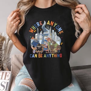 May include: Black t-shirt with a vibrant graphic of cartoon animal characters and the words "WHERE ANYONE CAN BE ANYTHING". The design incorporates a cityscape and stars.