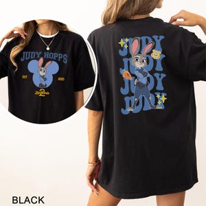 May include: Black t-shirt featuring Judy Hopps from Zootopia. The front design includes the text "JUDY HOPPS" above a cartoon image of Judy Hopps inside a blue Mickey Mouse-shaped design. The back features Judy Hopps in a police uniform.
