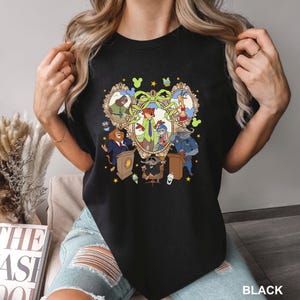 May include: Black crew neck t-shirt featuring a colorful cartoon graphic. The graphic includes framed portraits of animal characters, a central group of characters, and the word "BLACK" at the bottom right.