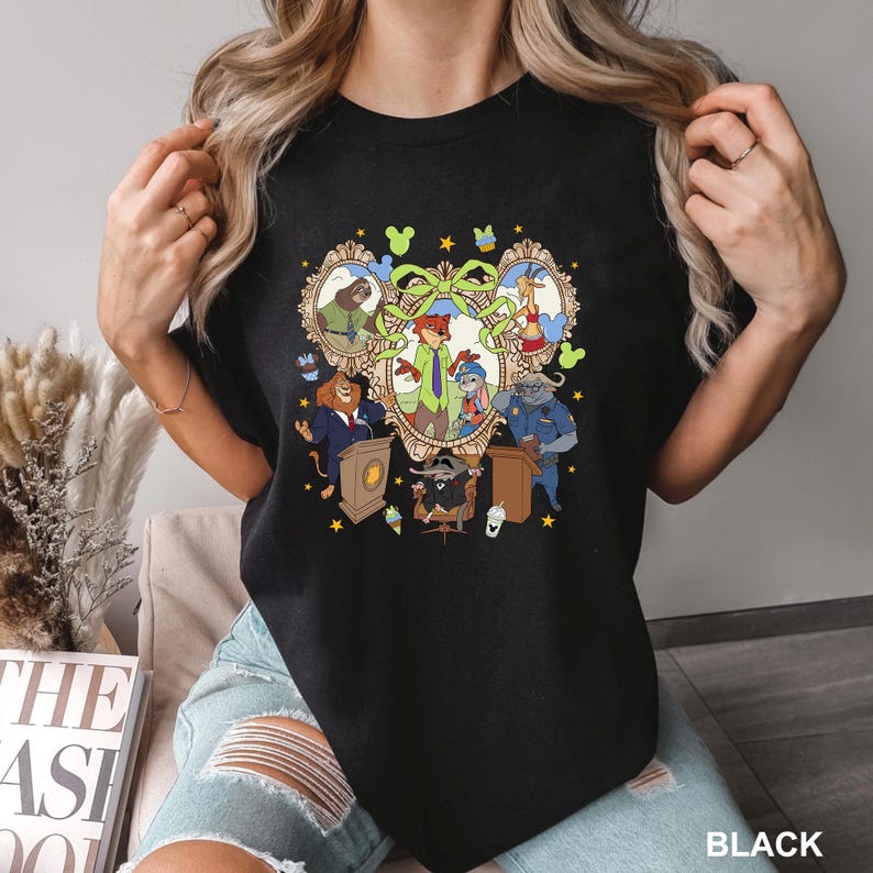 May include: Black crew neck t-shirt featuring a colorful cartoon graphic. The graphic includes framed portraits of animal characters, a central group of characters, and the word "BLACK" at the bottom right.