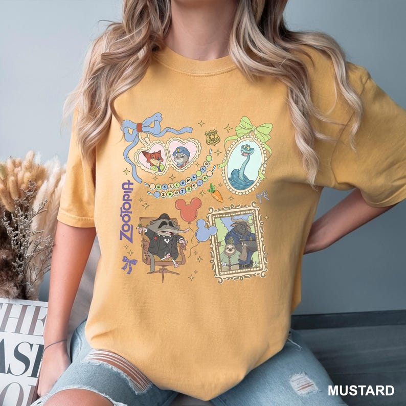 Puede incluir: Camiseta de color mostaza con un dise&ntilde;o de Zootopia. El gr&aacute;fico incluye ilustraciones enmarcadas de personajes como Nick Wilde y Judy Hopps. La palabra "Zootopia" est&aacute; impresa verticalmente en el lado izquierdo de la camiseta.