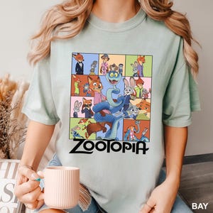 Puede incluir: Camiseta verde claro con un dise&ntilde;o gr&aacute;fico colorido de personajes de la pel&iacute;cula "Zootopia". El dise&ntilde;o presenta varios personajes de animales en una cuadr&iacute;cula, con la palabra "Zootopia" en letras negras en negrita.