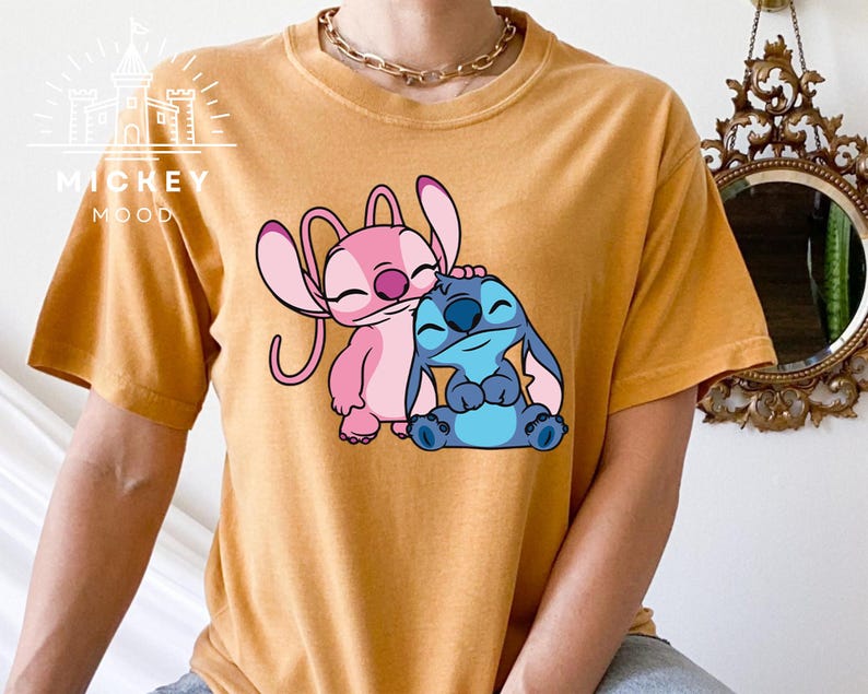 May include: A mustard yellow t-shirt with a graphic of Stitch and Angel from the Disney movie Lilo & Stitch. Stitch is blue and Angel is pink.