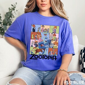 Puede incluir: Una camiseta azul b&iacute;garo con un gr&aacute;fico colorido de la pel&iacute;cula animada "Zootr&oacute;polis". El dise&ntilde;o incluye varios personajes de la pel&iacute;cula, con la palabra "ZOOTOPIA" en letras negras en la parte inferior.