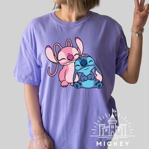 May include: Purple t-shirt with a pink and blue Stitch and Angel graphic. The graphic shows Stitch hugging Angel. The shirt has the text "MICKEY" printed on the bottom.