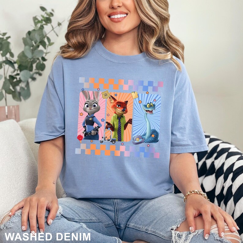 Puede incluir: Camiseta azul claro con personajes de dibujos animados: un conejo, un zorro y una serpiente. La camiseta tiene un estampado de cuadros y las palabras "WASHED DENIM" en la parte inferior. La camiseta es de estilo casual y c&oacute;modo.