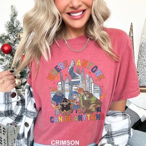 May include: Crimson t-shirt with a graphic that reads "WHERE ANYONE CAN BE ANYTHING" above a cartoon illustration of animal characters and city buildings. The shirt is a short-sleeved crew neck.