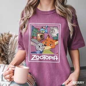 May include: Berry-colored t-shirt featuring a graphic from the animated film "Zootopia." The graphic includes characters Judy Hopps, Nick Wilde, and others, with the film's title in white. The shirt is a short-sleeved crew neck.