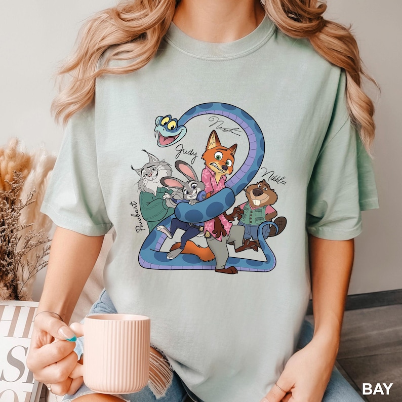 K&ouml;nnte beinhalten: Hellgr&uuml;nes T-Shirt mit einer Cartoon-Illustration von Zootopia-Charakteren. Das Design umfasst Nick, Judy und andere Charaktere, mit der Zahl "2" und den Namen der Charaktere. Das T-Shirt besteht aus einem weichen, bequemen Material.