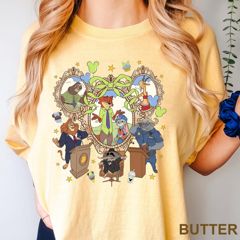 May include: Yellow t-shirt with a colorful cartoon graphic featuring animal characters in suits and uniforms. The graphic includes a fox, bunny, sloth, and other animals in a decorative frame. The word "BUTTER" is printed at the bottom.