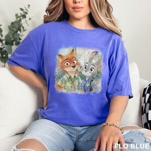 May include: A blue t-shirt featuring a graphic of Nick Wilde and Judy Hopps from Zootopia. The cartoon characters are in the center of the shirt. The text "FLO BLUE" is at the bottom right of the image.