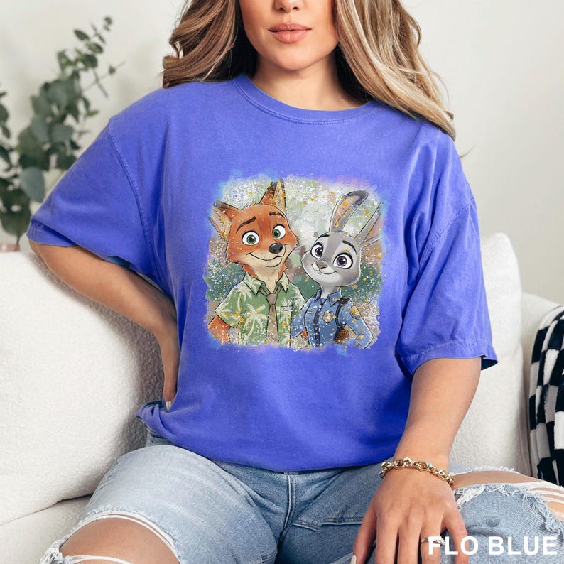 May include: A blue t-shirt featuring a graphic of Nick Wilde and Judy Hopps from Zootopia. The cartoon characters are in the center of the shirt. The text "FLO BLUE" is at the bottom right of the image.