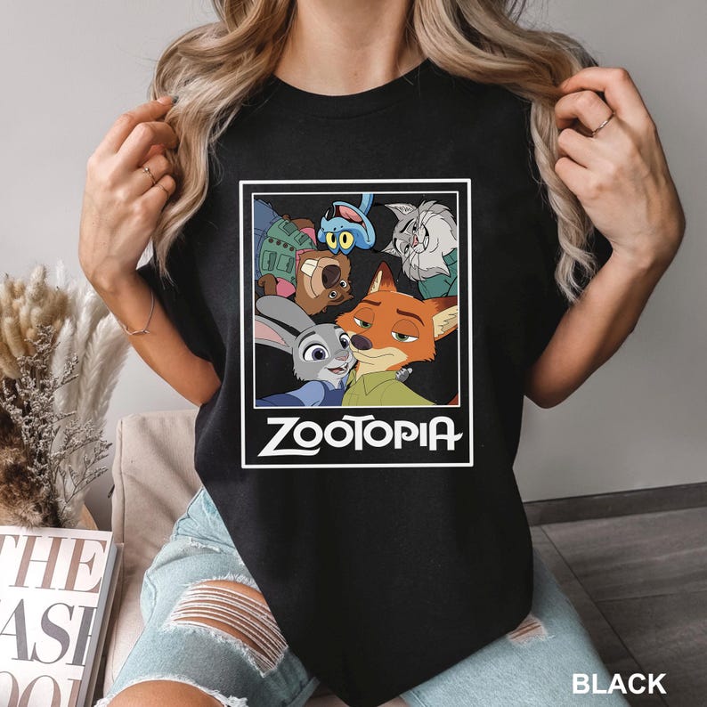 May include: Black t-shirt featuring a colorful graphic from the animated movie "Zootopia." The design includes characters like Judy Hopps, Nick Wilde, and others, framed by a white border with the movie title. The word "BLACK" is printed at the bottom.