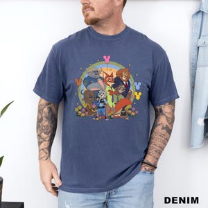 May include: A navy blue t-shirt featuring a colorful graphic of cartoon animal characters. The design includes a rabbit, fox, lion, and other characters, surrounded by flowers and Mickey Mouse icons. The shirt is made of soft material.