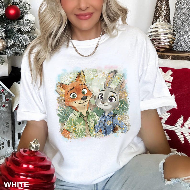 May include: White t-shirt featuring a colorful graphic of Nick Wilde and Judy Hopps from Zootopia. Nick is wearing a green shirt, and Judy is in a police uniform. The shirt has a crew neck and short sleeves.