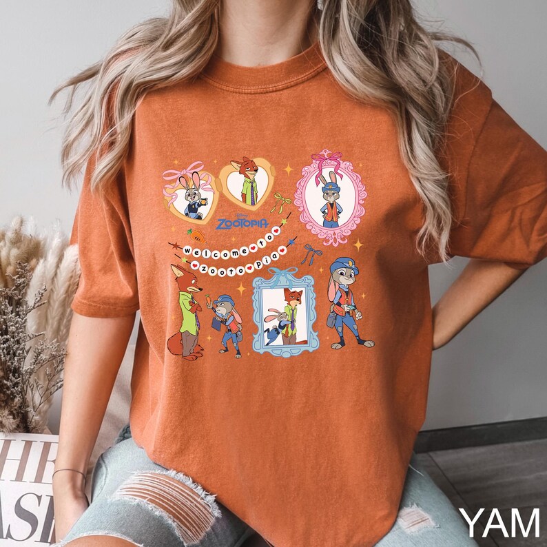 May include: Burnt orange t-shirt with a Zootopia design. The graphic includes framed portraits of Judy Hopps and Nick Wilde, the word "Zootopia", and the phrase "Welcome to Zootopia". The shirt is a warm, autumnal colour.