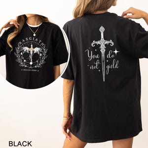 Może przedstawiać: Czarny t-shirt z białymi grafikami. Prz&oacute;d przedstawia okrągły wz&oacute;r z napisem "BASGIATH WAR COLLEGE" i "DRAGON RIDER". Tył prezentuje wz&oacute;r miecza ze słowami "You do not yield".