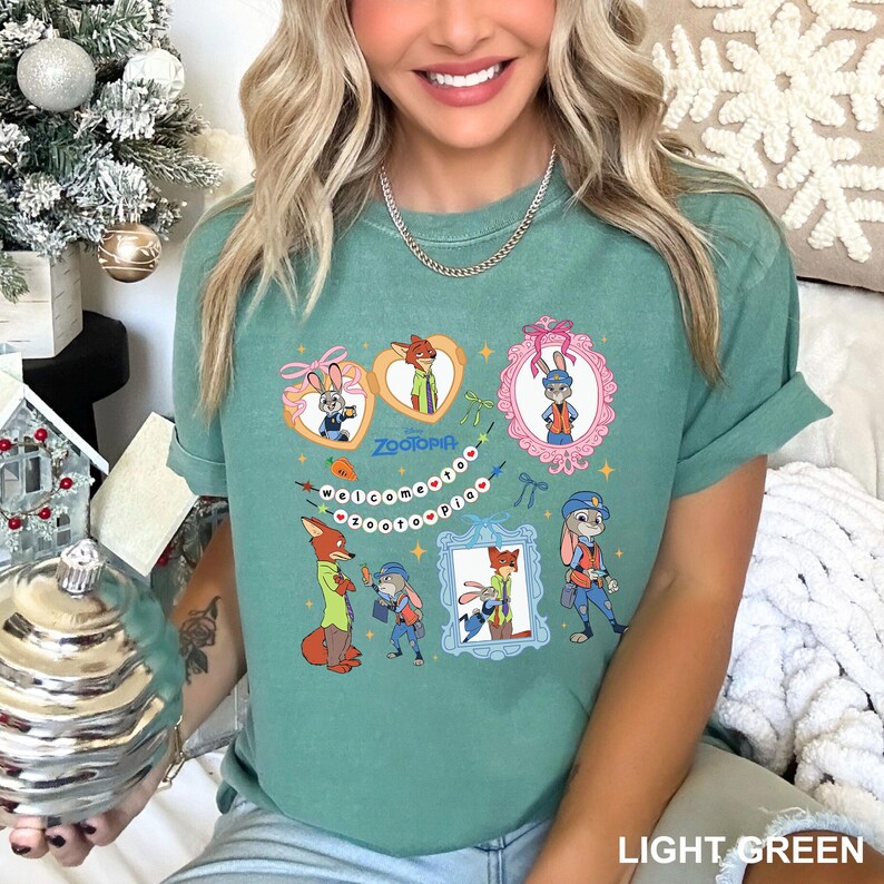 May include: Light green t-shirt with cartoon characters from Zootopia. The design includes images of a fox and a rabbit in various poses, framed in hearts and ornate frames. The word "Zootopia" is also visible.