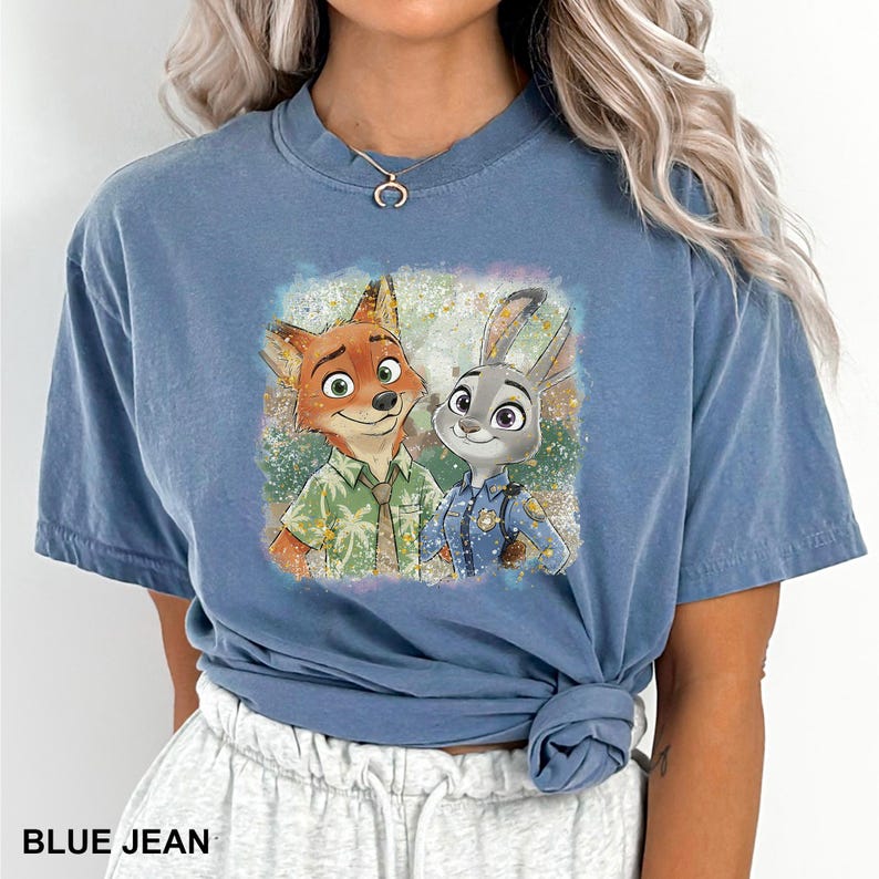 May include: Blue jean colored t-shirt featuring a colorful graphic of Nick Wilde and Judy Hopps from Zootopia. The image shows the characters smiling, with Nick in a green shirt and Judy in a police uniform. The text "BLUE JEAN" is at the bottom.