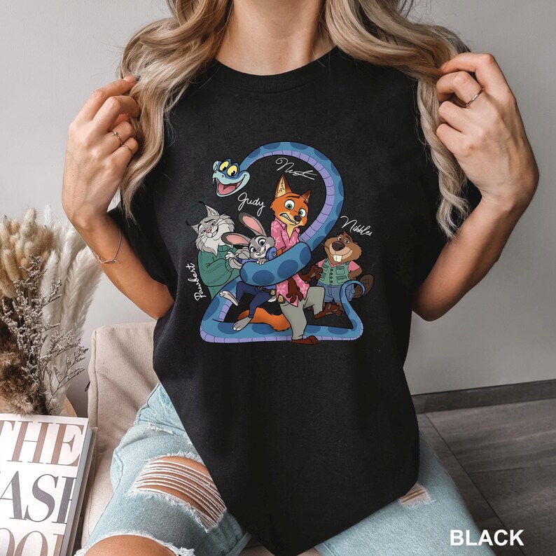 K&ouml;nnte beinhalten: Schwarzes T-Shirt mit einer Cartoon-Grafik von Filmfiguren. Die Grafik zeigt eine blaue Schlange mit den Namen "Nash", "Judy" und "Nibble". Auf dem Shirt steht auch das Wort "Black" unten rechts.