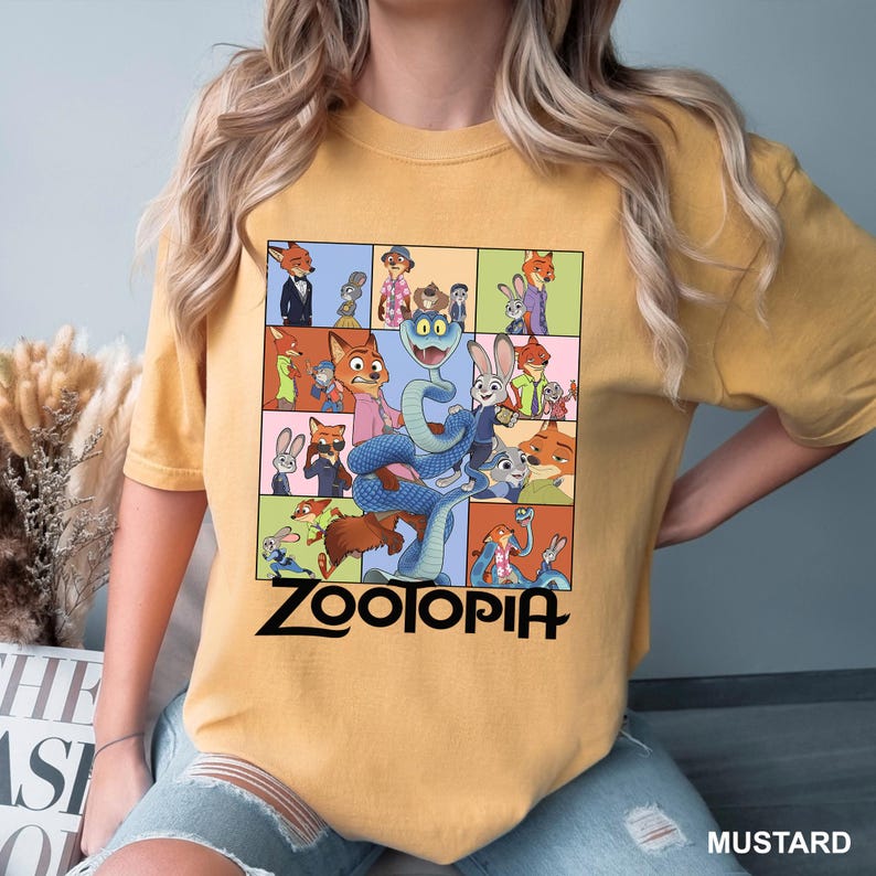 Puede incluir: Camiseta de color mostaza con un gr&aacute;fico colorido de personajes de la pel&iacute;cula animada "Zootopia". El dise&ntilde;o incluye una serpiente, un zorro y un conejo, con la palabra "Zootopia" en letras negras. La camiseta es de estilo casual.
