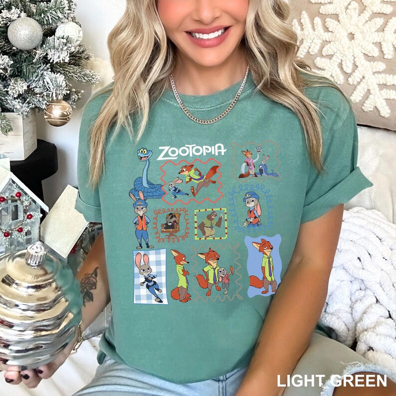 May include: Light green t-shirt featuring the word "ZOOTOPIA" above a grid of cartoon character illustrations. The shirt has short sleeves and a crew neck. The bottom right corner of the shirt has the words "LIGHT GREEN".