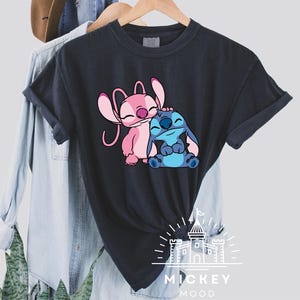 May include: Black t-shirt with a pink and blue cartoon Stitch and Angel design. The text "MICKEY MOOD" is printed below the characters.
