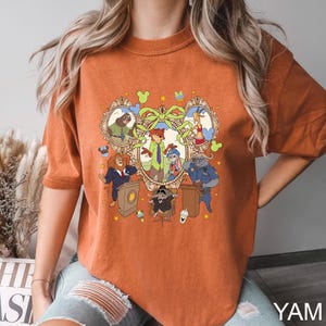 May include: Burnt orange t-shirt featuring a colorful cartoon graphic of various animal characters in a decorative frame. The graphic includes a fox, bunny, lion, and other animals. The text "YAM" is printed in white at the bottom right.