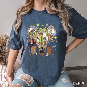 May include: A denim blue t-shirt featuring a colorful cartoon graphic of characters from a popular animated movie. The graphic includes a heart-shaped frame with various animal characters, including a fox, rabbit, and lion. The word "DENIM" is printed at the bottom right.