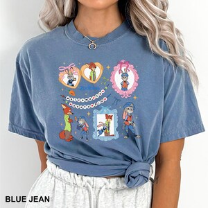May include: Blue jean coloured t-shirt featuring cartoon characters from the film Zootopia. The design includes framed images of the characters, the word "Zootopia", and the phrase "Welcome to Zootopia".