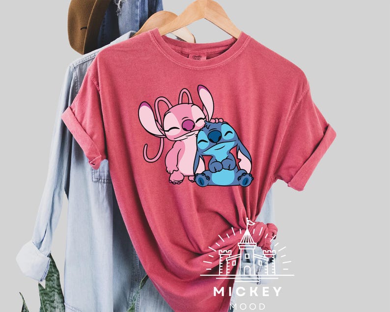 May include: A red t-shirt with a graphic of Stitch and Angel from Lilo & Stitch. The graphic shows Stitch hugging Angel. The shirt has the text "Mickey Mood" on the bottom.