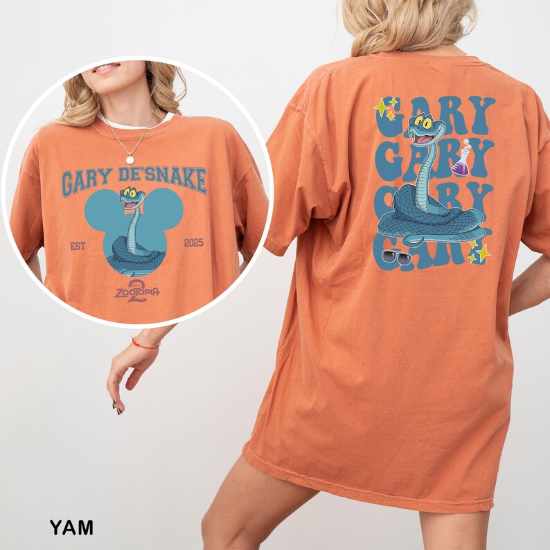 May include: Orange t-shirt with a cartoon snake design. The front features the text "GARY DE'SNAKE" above a blue snake illustration. The back of the shirt repeats the text and snake design. The shirt includes the text "Zootopia 2" and the year "2025".