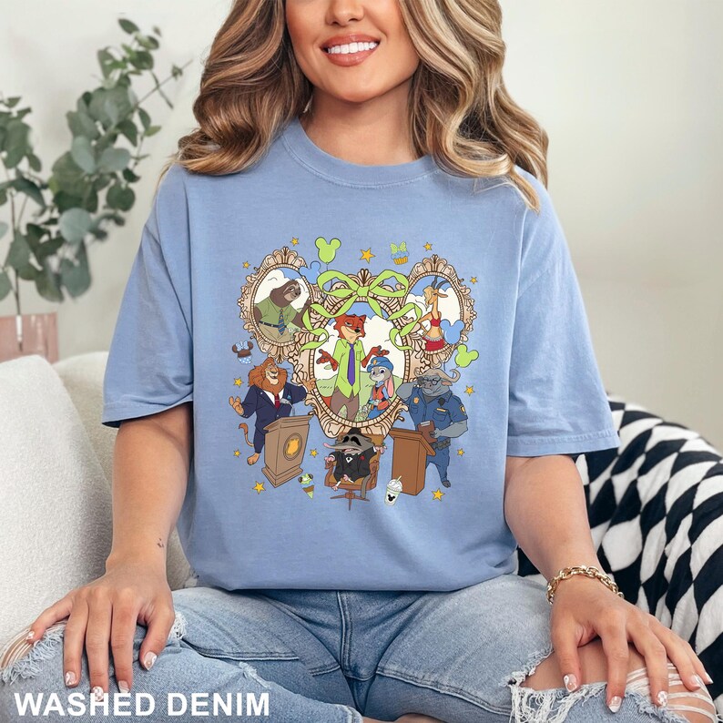 May include: A light blue t-shirt with a cartoon graphic featuring animal characters in a heart-shaped frame. The shirt has the words "WASHED DENIM" printed at the bottom.