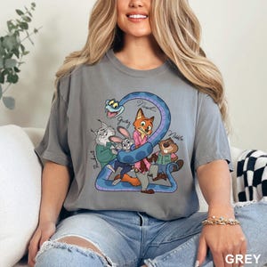 K&ouml;nnte beinhalten: Graues T-Shirt mit einem farbenfrohen Cartoon-Motiv von Zootopia-Charakteren, darunter Judy Hopps und Nick Wilde, mit der Zahl 2. Die Namen der Charaktere sind auf dem Shirt geschrieben. Das Wort "GREY" ist unten aufgedruckt.