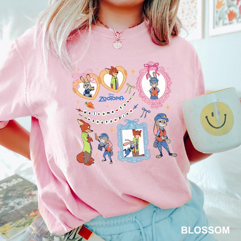 May include: Pale pink Zootopia graphic t-shirt with cartoon characters in ornate frames. The shirt features the text "Welcome to Zootopia" and the Disney Zootopia logo. The t-shirt is a light pink colour.