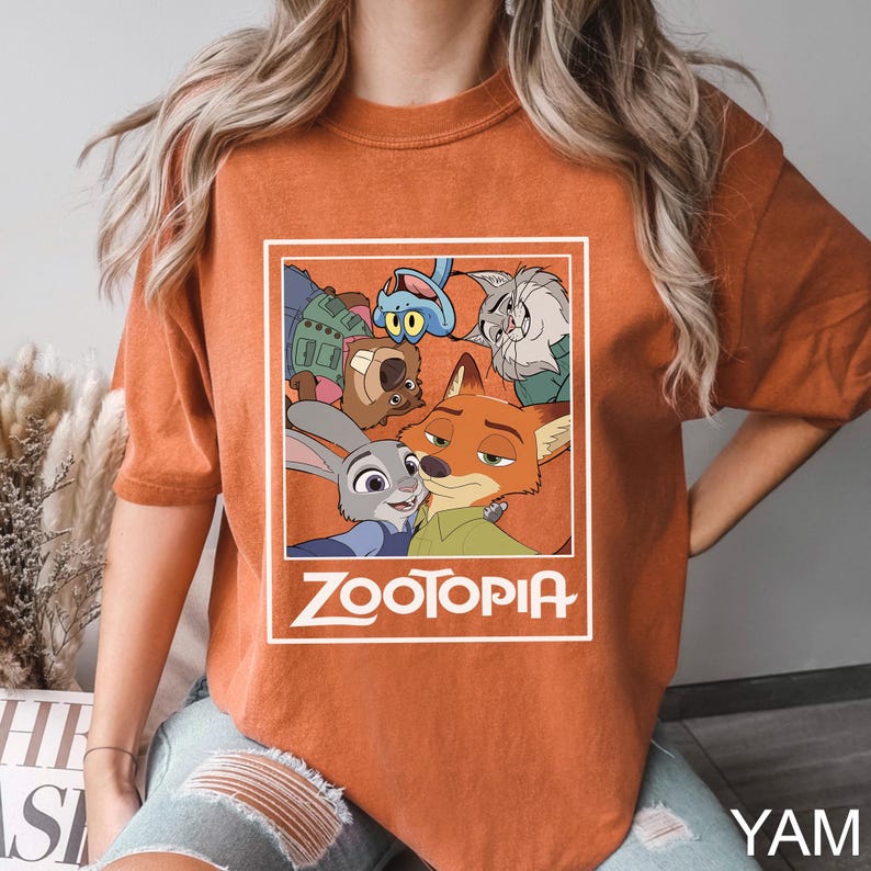 May include: Burnt orange t-shirt featuring a graphic from the animated film Zootopia. The graphic includes characters Judy Hopps, Nick Wilde, and others, with the film's title in white. The shirt is a comfortable, casual style.