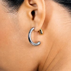 May include: A woman wearing two earrings. One is a large, silver hoop earring, and the other is a small, gold stud earring. The woman is wearing a diamond tennis necklace.