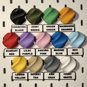 Puede incluir: Una colecci&oacute;n de 12 objetos decorativos coloridos, impresos en 3D, cada uno con un dise&ntilde;o arremolinado &uacute;nico. Los colores incluyen negro, verde, naranja, rojo, morado, rosa, azul, amarillo, beige, gris y blanco. Cada objeto tiene una etiqueta con su nombre de color.