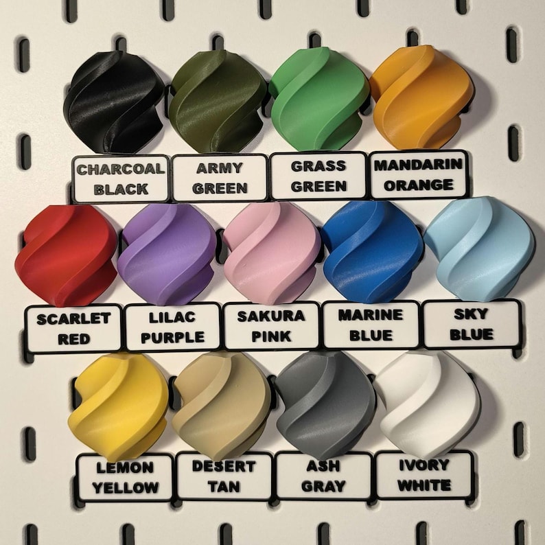 Puede incluir: Una colecci&oacute;n de 12 objetos decorativos coloridos, impresos en 3D, cada uno con un dise&ntilde;o arremolinado &uacute;nico. Los colores incluyen negro, verde, naranja, rojo, morado, rosa, azul, amarillo, beige, gris y blanco. Cada objeto tiene una etiqueta con su nombre de color.