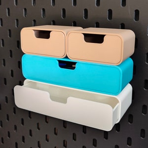 May include: Four colorful storage drawers in beige, teal, and white are mounted on a black pegboard. The drawers are rectangular with rounded edges and a recessed handle. The top two drawers are beige, the middle one is teal, and the bottom one is white.