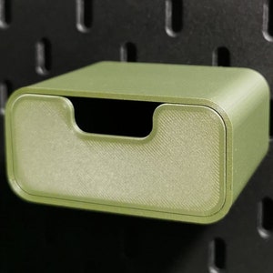 Puede incluir: Caja de almacenamiento rectangular verde oliva con frente curvo y asa empotrada. La caja est&aacute; montada en una panel perforado negro. Dise&ntilde;ada para guardar objetos peque&ntilde;os.