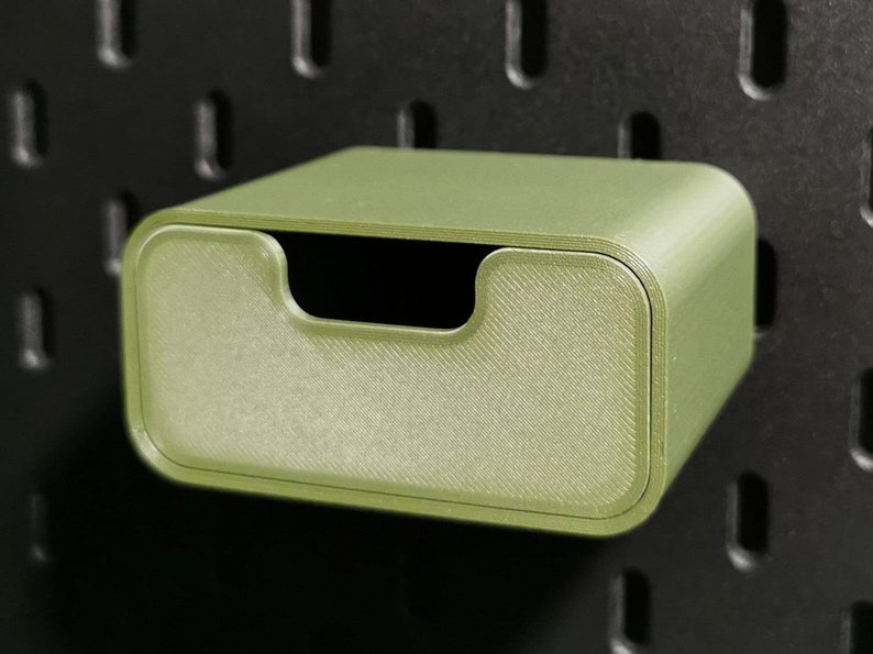 Puede incluir: Caja de almacenamiento rectangular verde oliva con frente curvo y asa empotrada. La caja est&aacute; montada en una panel perforado negro. Dise&ntilde;ada para guardar objetos peque&ntilde;os.
