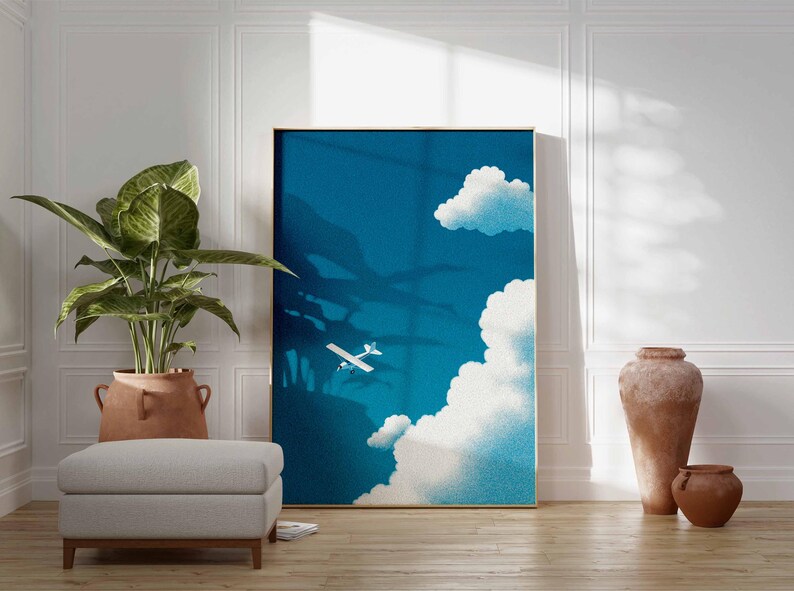 Peut inclure: Une affiche encadr&eacute;e repr&eacute;sente un avion traversant un ciel bleu avec des nuages blancs. L'&oelig;uvre est expos&eacute;e dans une pi&egrave;ce avec une grande plante en pot, un pouf gris et des poteries d&eacute;coratives.