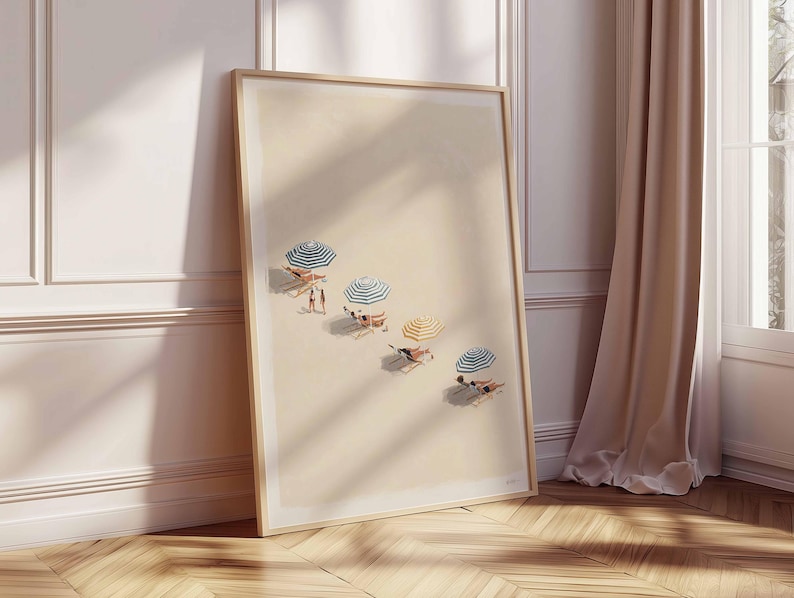 May include: A framed art print showing a beach scene with people under striped umbrellas. The artwork has a light colour palette and a wooden frame, leaning against a wall with a curtain and window. The beach umbrellas have blue and white stripes.