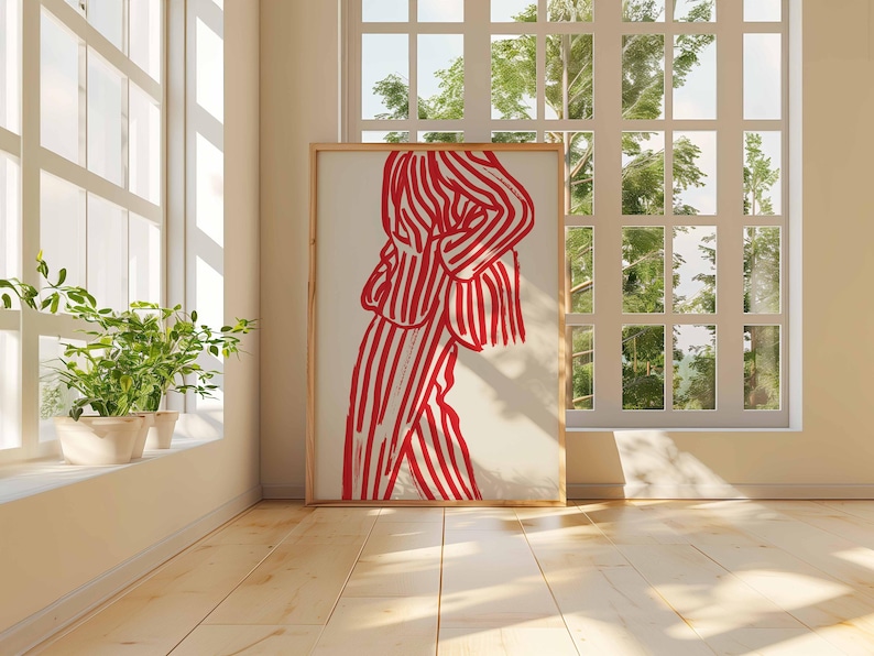 K&ouml;nnte beinhalten: Ein gerahmter Kunstdruck mit einer Figur in rot-wei&szlig; gestreifter Kleidung. Das Kunstwerk wird in einem Raum mit Tageslicht, Holzboden und einem Fenster mit Blick auf Gr&uuml;n pr&auml;sentiert. Der Rahmen ist hellbraun.