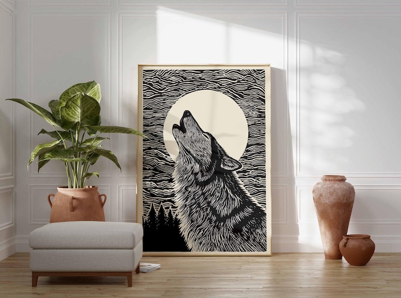 May include: A framed black and white art print shows a howling wolf against a full moon and a textured sky. The artwork is displayed in a room with a large potted plant, a grey ottoman, and decorative pottery.