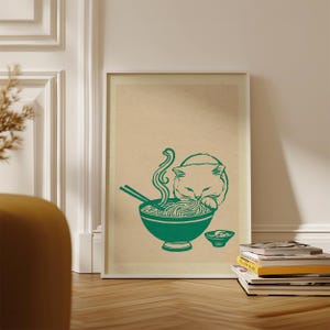 May include: A framed wall art print featuring a green line drawing on a beige background. The illustration depicts a cat eating noodles from a bowl with chopsticks, with steam rising from the food and a small side dish placed next to the bowl.