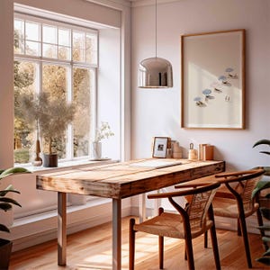 May include: A light-filled home office featuring a wooden desk and two woven chairs. A framed print of a beach scene adorns the wall. A large window provides a view of trees. A silver pendant light hangs above the desk.