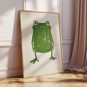 May include: A framed print of a green frog with a white background. The frog is stylized and has a simple design.