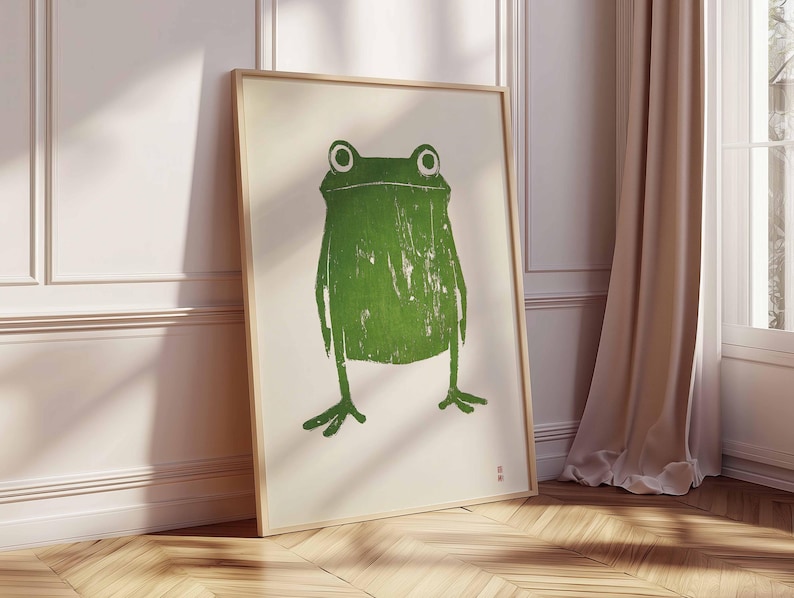 May include: A framed print of a green frog with a white background. The frog is stylized and has a simple design.